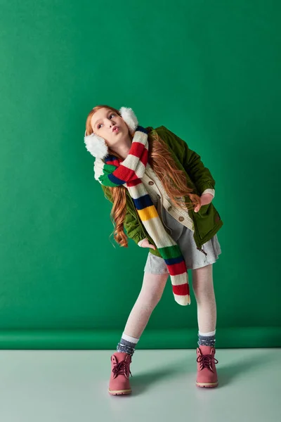 Full length, preteen girl in ear muffs, striped scarf and winter outfit pouting lips on turquoise — Stock Photo