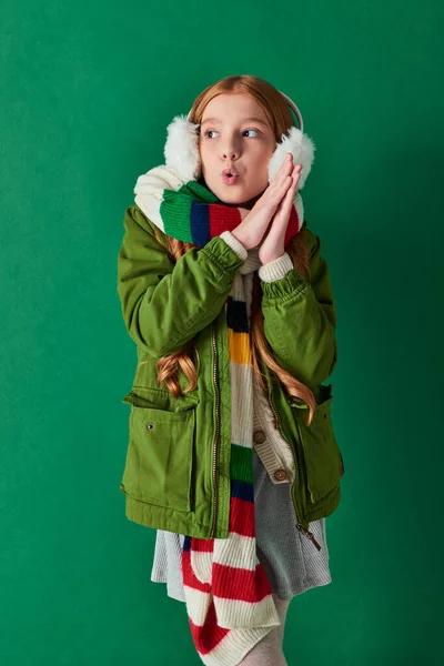 Preteen menina no ouvido muffs, cachecol listrado e roupa de inverno sentindo frio no pano de fundo turquesa — Fotografia de Stock