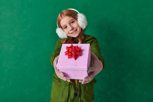 Focus on pink Christmas present with red bow, happy preteen girl in winter outfit with gift — Stock Photo