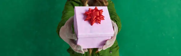 Focus sur le cadeau de Noël rose avec arc rouge, fille coupée en gants d'hiver tenant cadeau enveloppé — Photo de stock