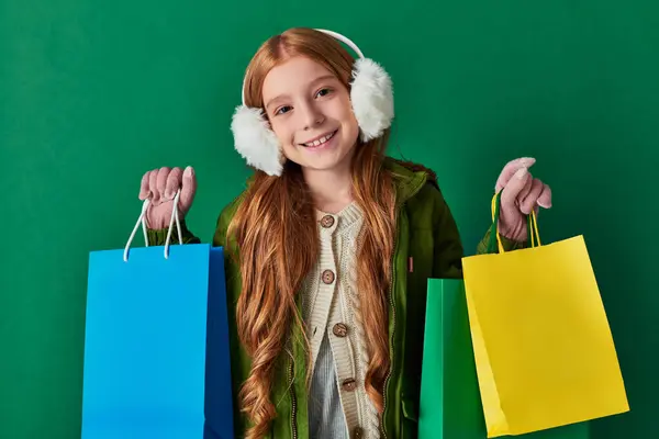 Preto sexta-feira e temporada de férias, menina feliz em roupa de inverno e abafadores de ouvido olhando para sacos de compras — Fotografia de Stock