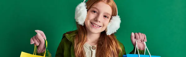 Bannière de la saison des fêtes, heureuse préadolescente en tenue d'hiver et cache-oreilles tenant des sacs à provisions — Photo de stock
