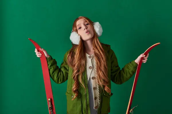 Kalte Luft, Frühchen in Ohrenschützern und Winteroutfit atmet und hält rote Skier auf Türkis — Stockfoto