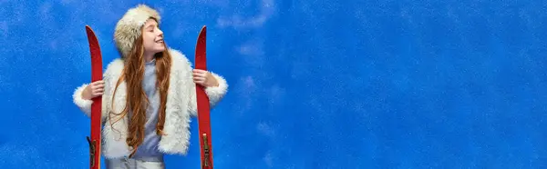 Winterfreude, zufriedenes Mädchen in Kunstpelzjacke und Hut mit roten Skiern auf Türkis, Banner — Stockfoto