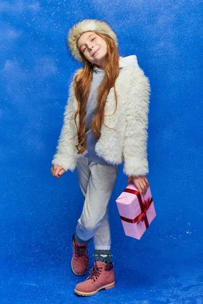 Зимняя страна чудес, счастливая девушка в искусственной меховой куртке и шляпе с подарочной коробкой на бирюзовом фоне — стоковое фото