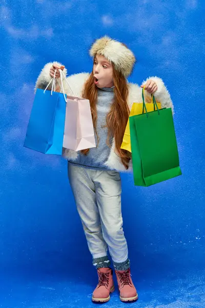 Shopping di festa, scioccato ragazza in giacca di pelliccia sintetica che tiene borse della spesa su sfondo turchese — Foto stock
