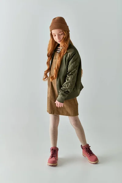 Милая девочка-подросток с длинными волосами, стоящими в шляпе, платье и зимняя куртка и сапоги на сером фоне — стоковое фото
