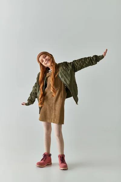 Счастливая дочка с длинными волосами, стоящая с протянутыми руками на сером заднике, мода ветреная — стоковое фото
