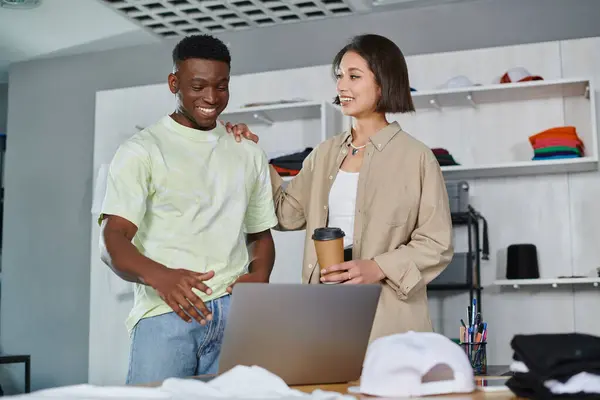 Zufriedene asiatische Frau berührt Schulter eines afrikanisch-amerikanischen Kollegen in der Nähe von Laptop im Druckstudio — Stockfoto