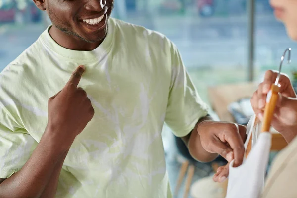Vista cortada de homem americano africano sorridente tocando sua t-shirt e roupas na mão do colega — Fotografia de Stock
