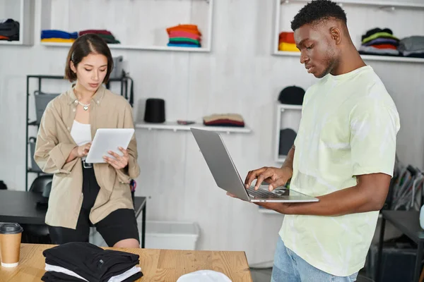 Jóvenes emprendedores interracial con portátil y tableta digital trabajando en la puesta en marcha en estudio de impresión - foto de stock
