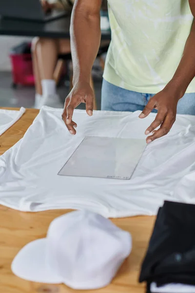 Vista parcial del diseñador afroamericano sosteniendo plantilla de formato transparente cerca de la camiseta blanca - foto de stock