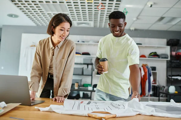 Happy multiethnic fashion designers looking at clothing with format sizes in print studio, teamwork — Stock Photo