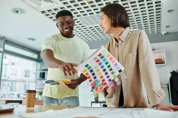 Sorridente afro-americano designer apontando para a paleta de cores perto asiático colega no estúdio de impressão — Fotografia de Stock