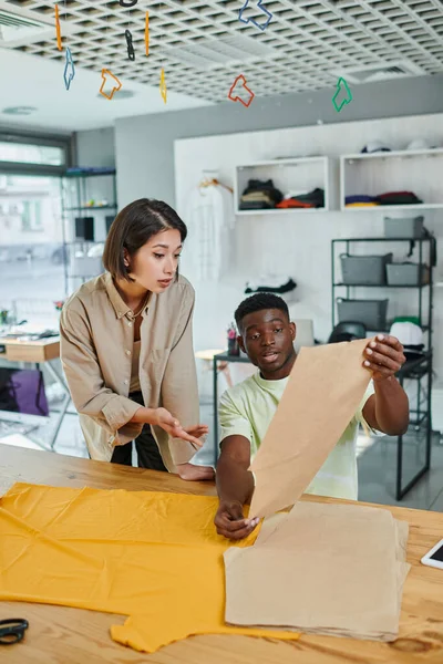 Young interracial fashion designers working with sewing patterns in print studio, creativity — Stock Photo