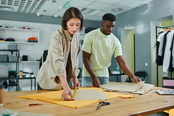 Skilled interracial fashion designers measuring sewing patterns in print studio, small business — Stock Photo