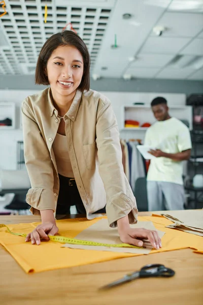 Alegre asiático designer medição costura padrão e olhando para câmera no print studio, felicidade — Fotografia de Stock