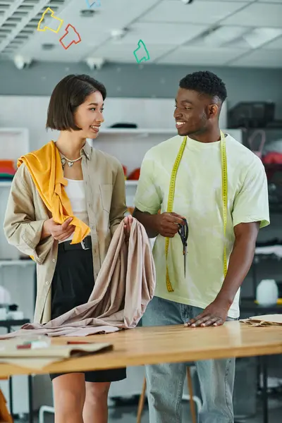 Multiethnic designers with fabric samples and measuring tape smiling at each other in print studio — Stock Photo