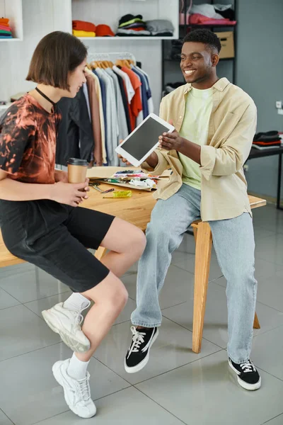 Alegre designer afro-americano mostrando tablet digital para colega asiático em oficina de impressão têxtil — Fotografia de Stock