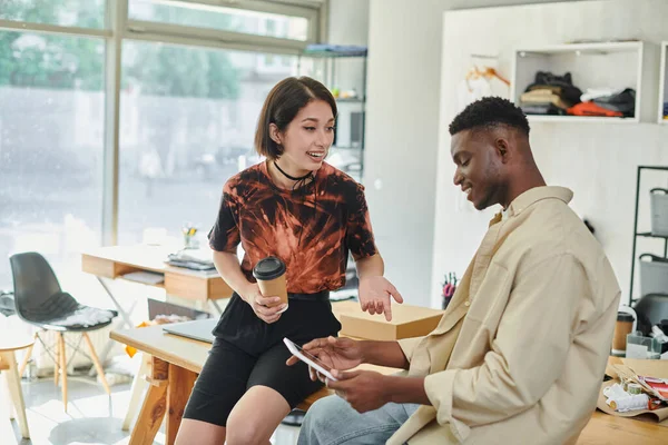 Asiático designer com copo de papel falando com africano americano colega com digital tablet no atelier — Fotografia de Stock