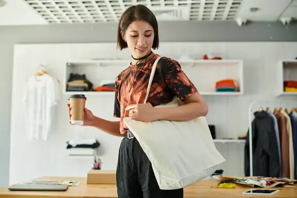 Успішний азіатський дизайнер з полотном сумка для покупок і кави, щоб піти в сучасну друкарню студію — стокове фото