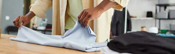 Cropped view of professional african american worker folding clothing in print atelier, banner — Stock Photo