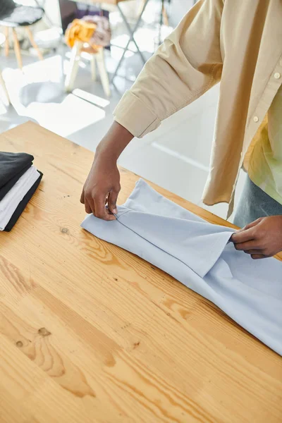 Partial view of young skilled african american man folding clothes carefully in modern print studio — Stock Photo