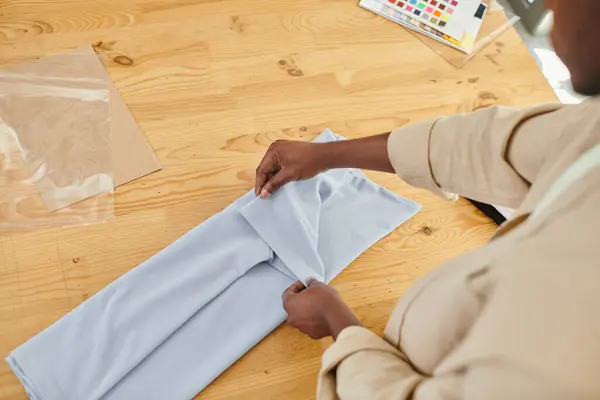 Vista recortada de hombre afroamericano experimentado plegando la ropa cuidadosamente en la mesa en el estudio de impresión - foto de stock