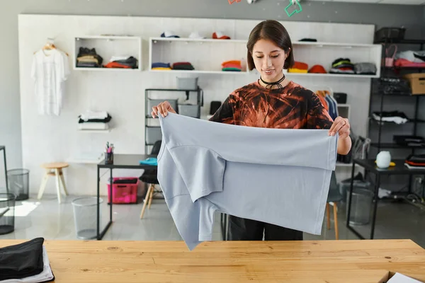 Feliz e habilidoso asiático mulher dobrar roupas com cuidado no têxtil imprimir estúdio, pequeno negócio — Fotografia de Stock