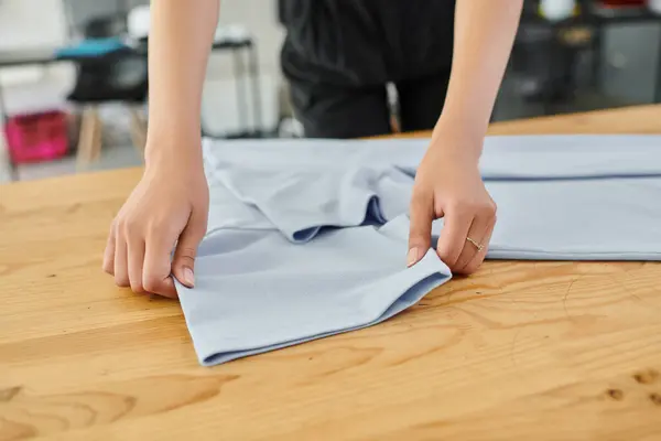 Cropped view of professional woman working in textile print workshop and folding clothes neatly — Stock Photo