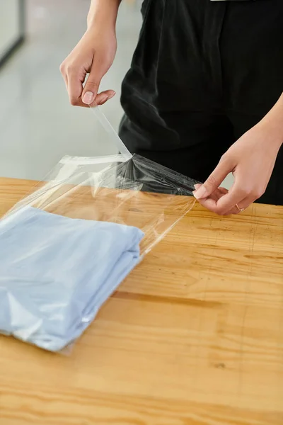 Vue partielle de travailleuse diligente emballant des vêtements pliés dans un sac en plastique dans un studio d'impression textile — Photo de stock