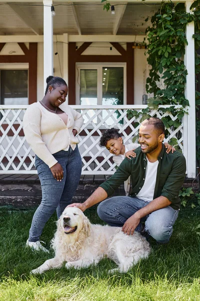 Familia afroamericana alegre jugando con el perro en el patio trasero de su casa, tiempo de calidad - foto de stock