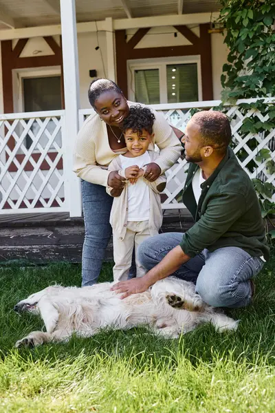 Веселі афроамериканські батьки і син грають з собакою на задньому дворі свого будинку, якісний час — стокове фото