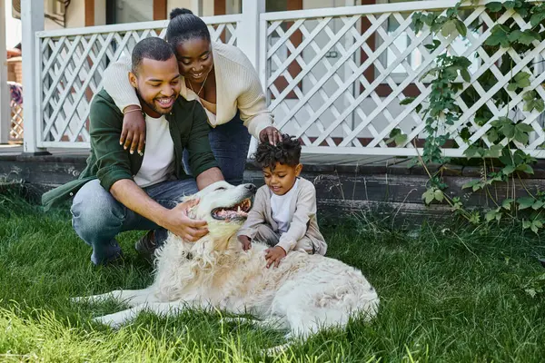 Позитивні афроамериканські батьки і син грають з собакою на задньому дворі свого будинку, якісний час — стокове фото