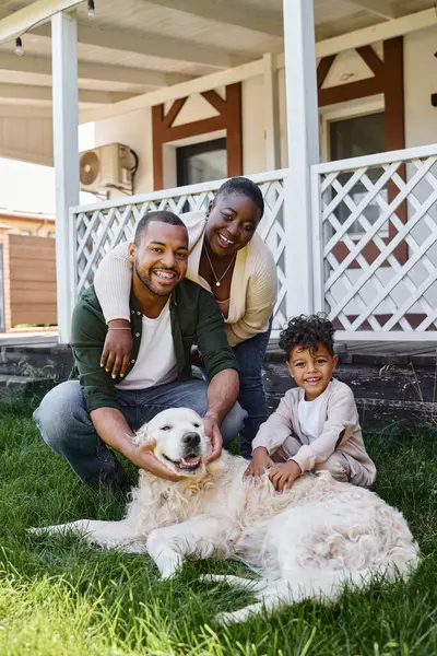 Foto de familia, los padres afroamericanos positivos y el hijo jugando con el perro en el patio trasero de su casa - foto de stock