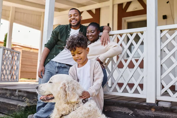 Positif enfant afro-américain jouer avec chien près des parents sur la cour de leur maison, temps de qualité — Photo de stock