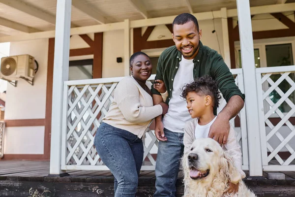 Familienfoto, glückliche afrikanisch-amerikanische Eltern und Sohn spielen mit Hund im Hinterhof ihres Hauses — Stockfoto