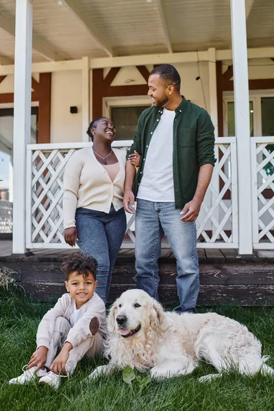 Momento familiar, alegres padres afroamericanos e hijo jugando con el perro en el patio trasero de su casa — Stock Photo