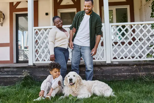 Сімейний час, щасливі афроамериканські батьки дивляться на сина, який грає з собакою на задньому дворі будинку — стокове фото