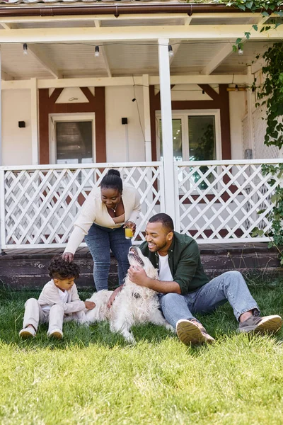 Tiempo de la familia, padres afroamericanos felices e hijo rizado jugando con el perro en el patio trasero de la casa — Stock Photo