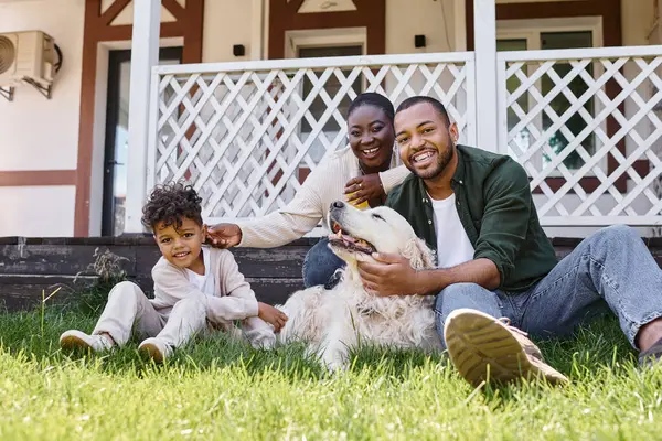 Tiempo de la familia, alegres padres afroamericanos y rizado hijo jugando con el perro en el patio trasero de la casa - foto de stock