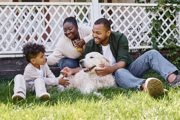 Tiempo de calidad, padres afroamericanos alegres e hijo rizado jugando con el perro en el patio trasero de la casa — Stock Photo