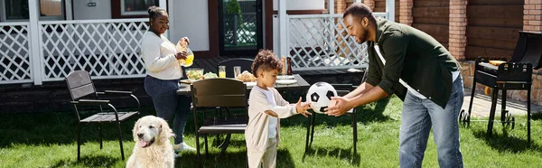 Family weekend banner, happy african american father giving soccer ball to son on backyard of house — Stock Photo