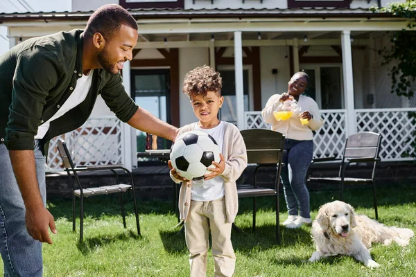 Familienwochenende, glücklicher afrikanisch-amerikanischer Vater schaut Sohn mit Fußballball bei Frau im Hinterhof an — Stockfoto