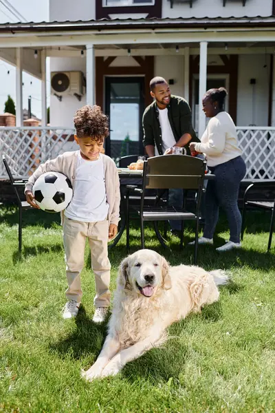 Tiempo familiar, niño afroamericano feliz celebración de fútbol cerca de los padres y el perro en el patio trasero de la casa — Stock Photo