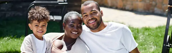 Familienporträt einer positiv afrikanisch-amerikanischen Familie, die in die Kamera blickt und auf dem Rasen sitzt, Banner — Stockfoto