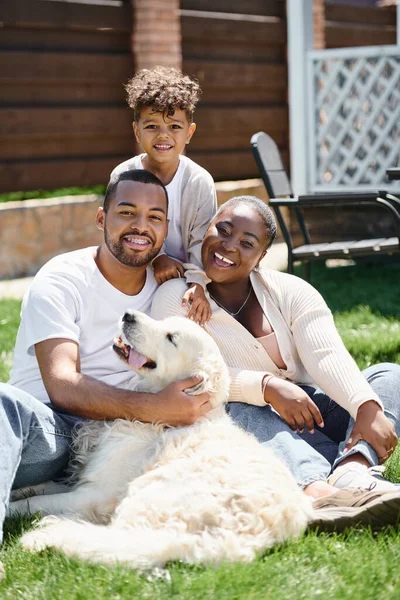 Tempo di qualità di genitori africani americani gioiosi e figlio sorridente e seduto sull'erba vicino al cane — Foto stock