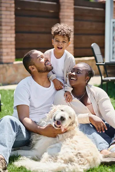 Quality time of happy african american parents and son smiling and sitting on grass near dog — Stock Photo