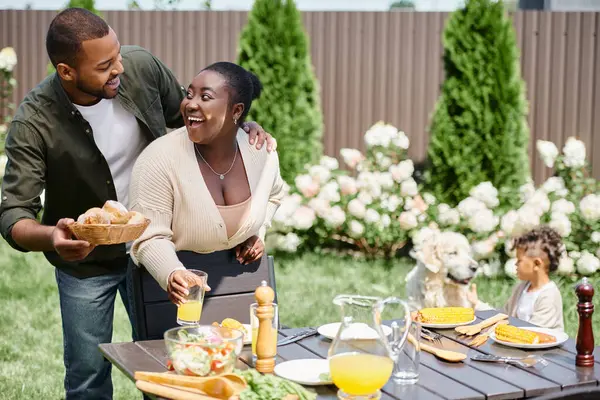 Happy african american married couple serving table in garden near son playing with dog on backyard — Stock Photo