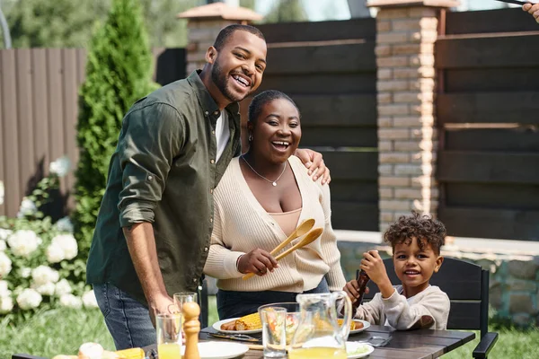 Portrait of cheerful african american parents and son preparing garden table for lunch on backyard — Stock Photo